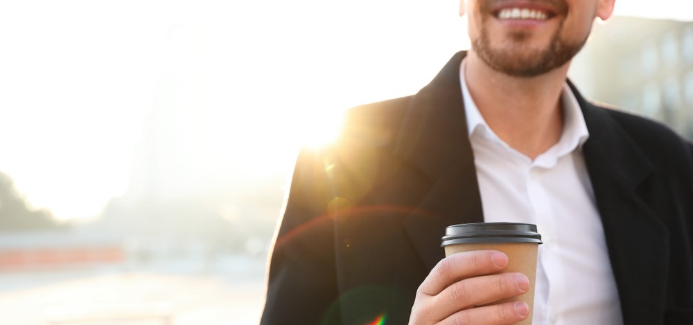 Man with cup of coffee on city street in morning, closeup | daily compliance management operational mode