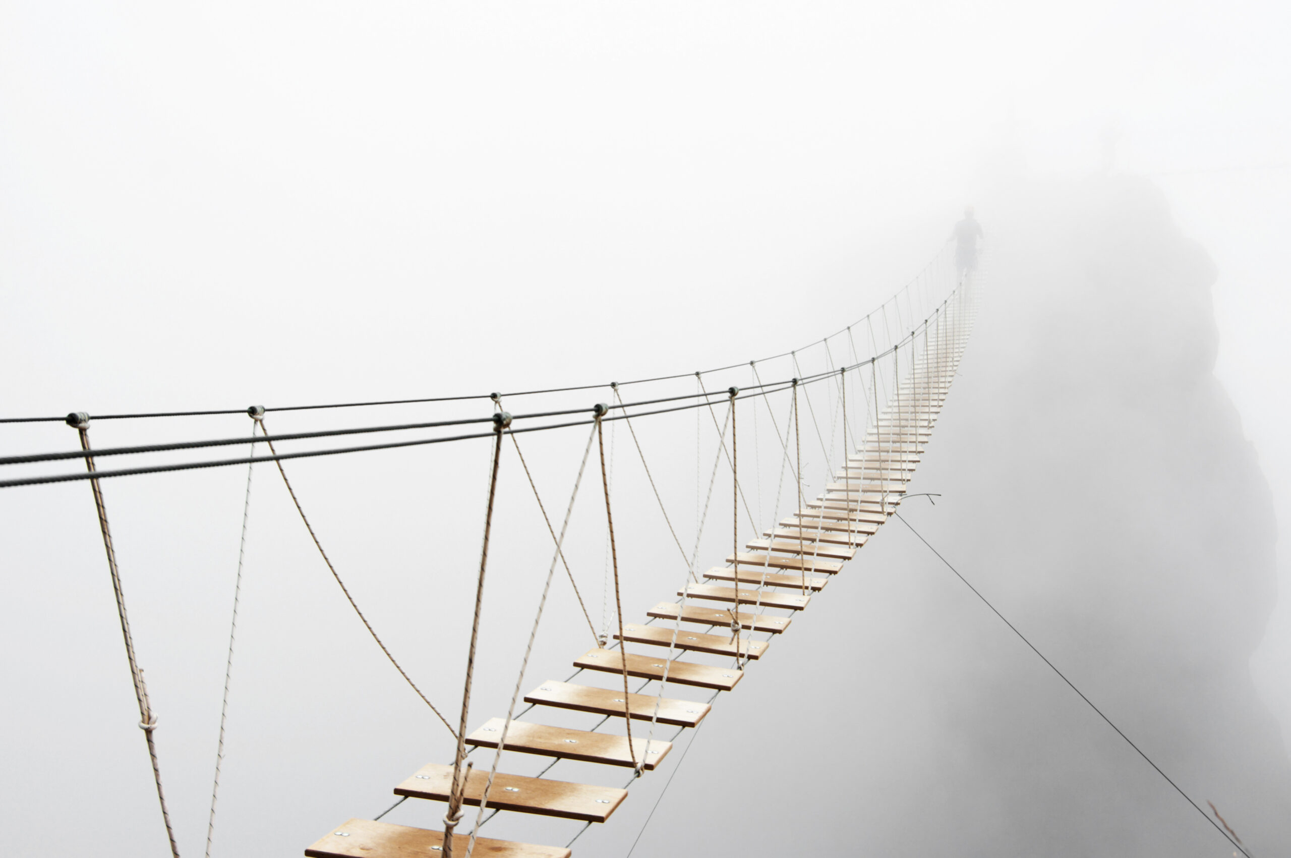 man walking on hanging bridge vanishing in fog | avoid mergers and acquisitions security and compliance pitfalls