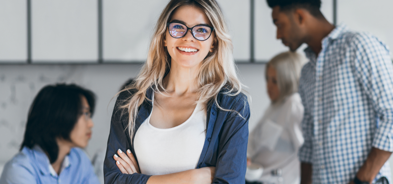 Female Assessor smiling while her client team is working in the background | how to find a compliance Assessor