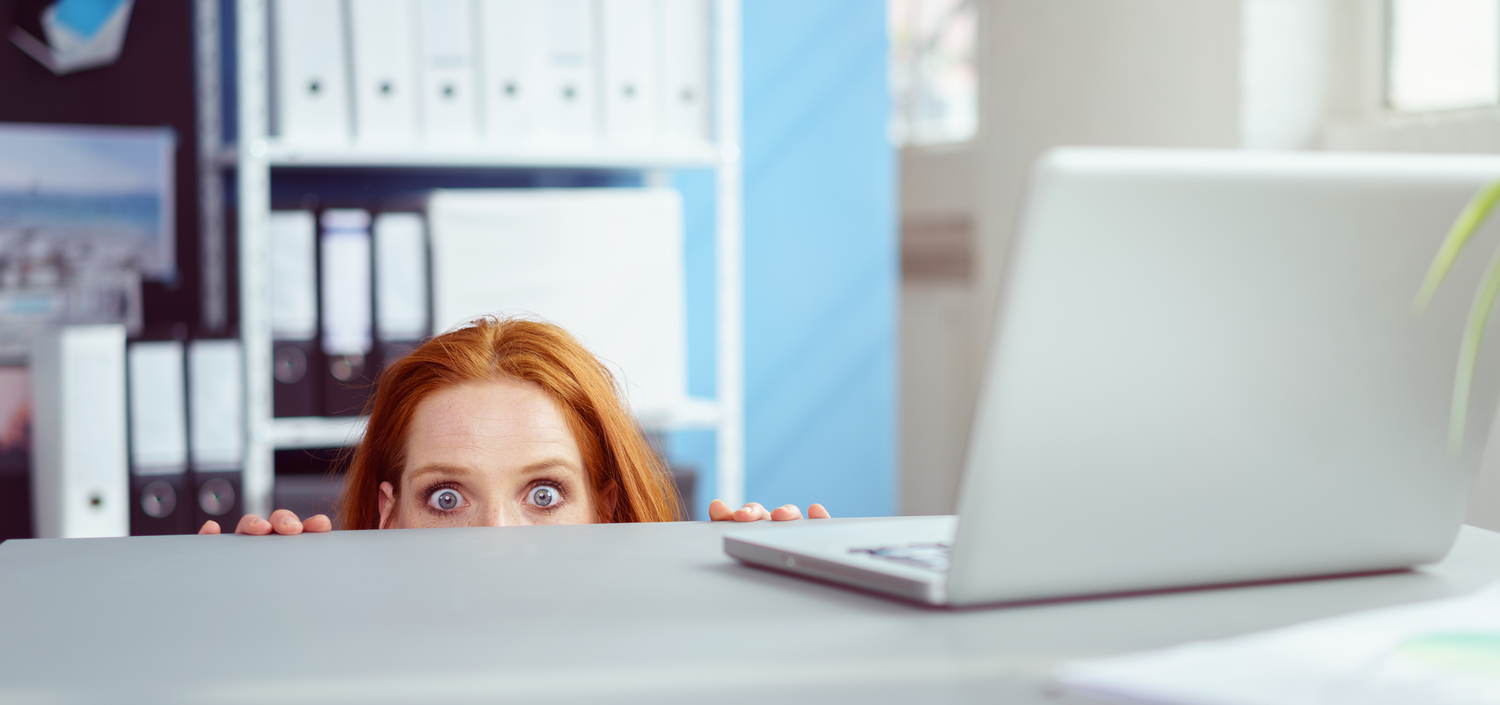 Business woman hiding behind her desk and avoiding get started with compliance