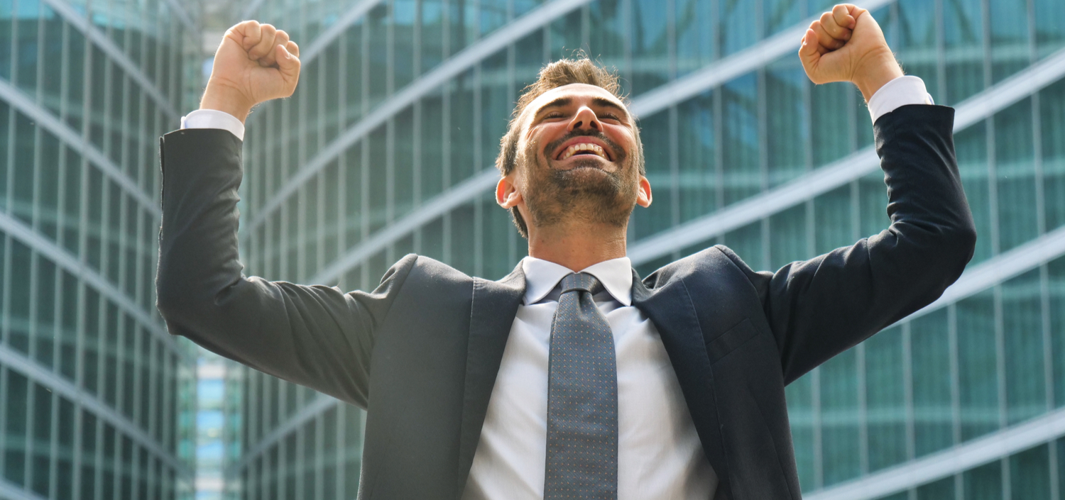 businessman celebrating by raising his hands in the air | make the business case for a compliance management system