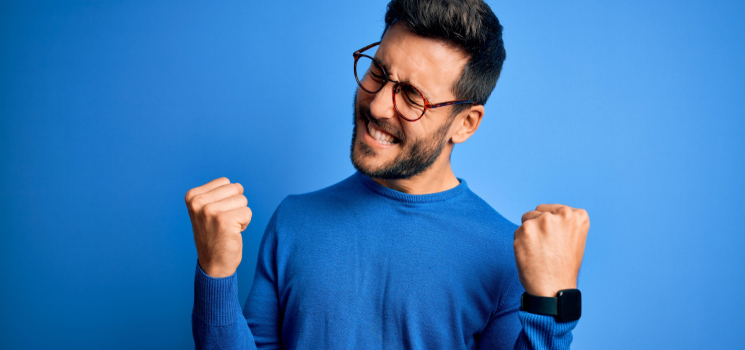 young man celebrating against a plain blue background | get up and running with CMMC compliance