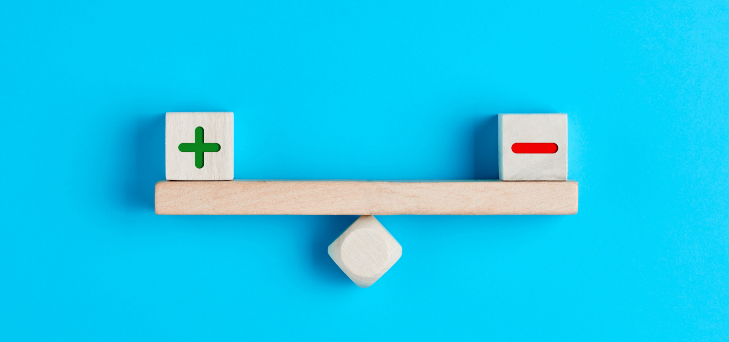 plus and minus symbols on wooden blocks balancing on a wooden seesaw | Buying a Compliance Management Solution