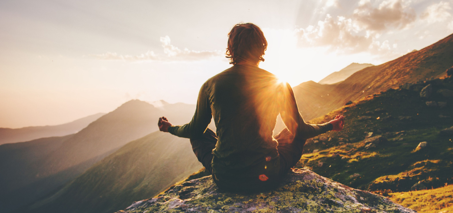 man meditating on a mountain at sunrise | compliance stress