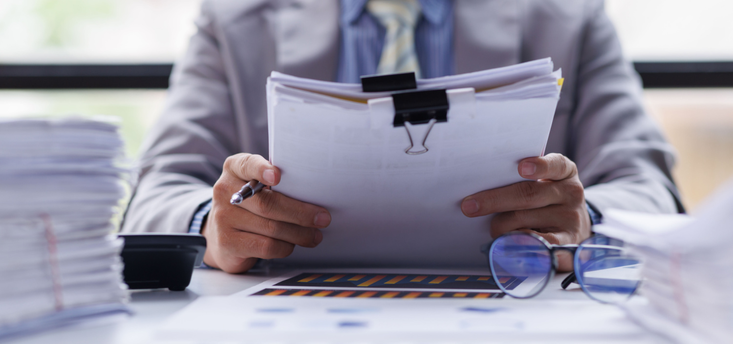 C3PAO sitting at a desk and holding a stack of papers | self-assessment vs third-party CMMC Assessor