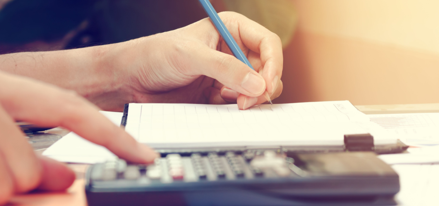 close-up of a woman’s hands as she uses a calculator and takes notes | cost of compliance