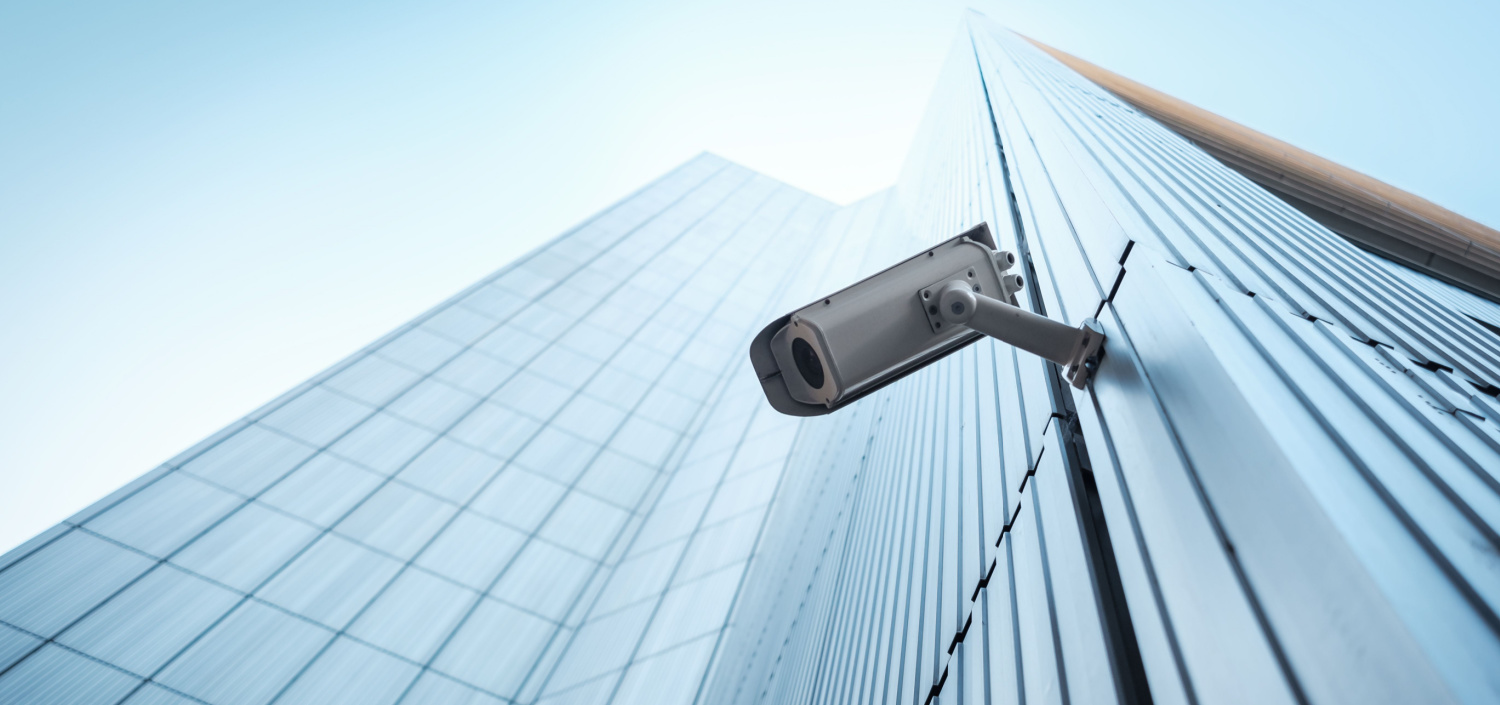 security camera mounted on the outside of a glass building | physical security and cybersecurity